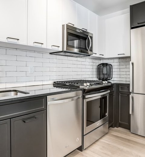 Financial District, NY Apartments for Rent - 63 Wall Street - Kitchen with Wood-Style Flooring, Stainless Steel Appliances, White and Black Cabinetry, and White Tile Backsplash.